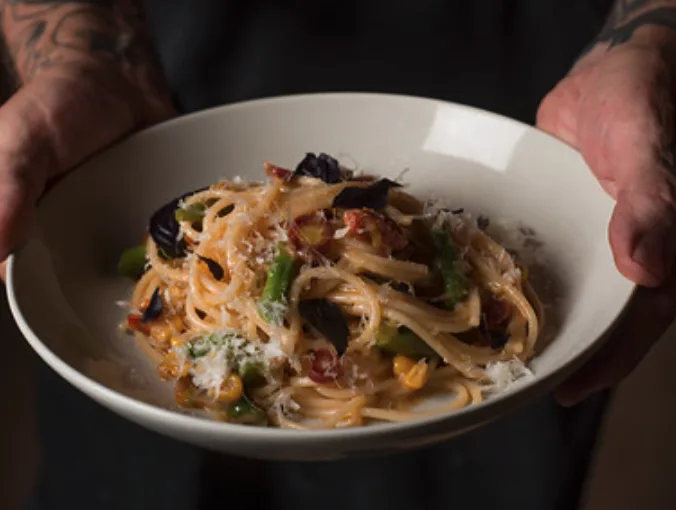 Chef presenting a seasonal pasta dish prepared by The Restaurant