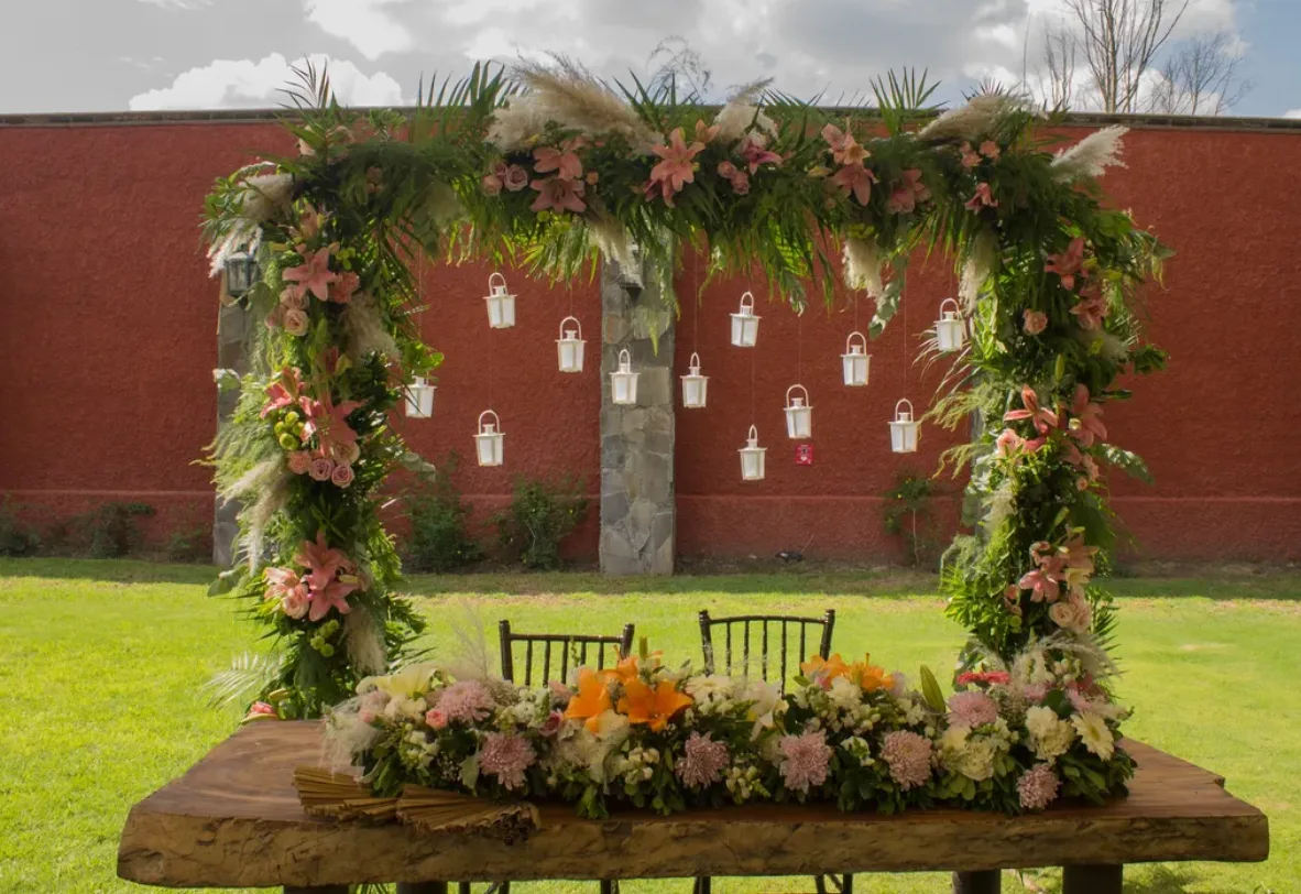 Garden wedding structure covered in lush greenery, pink flowers and hanging lanterns by Florería Florena