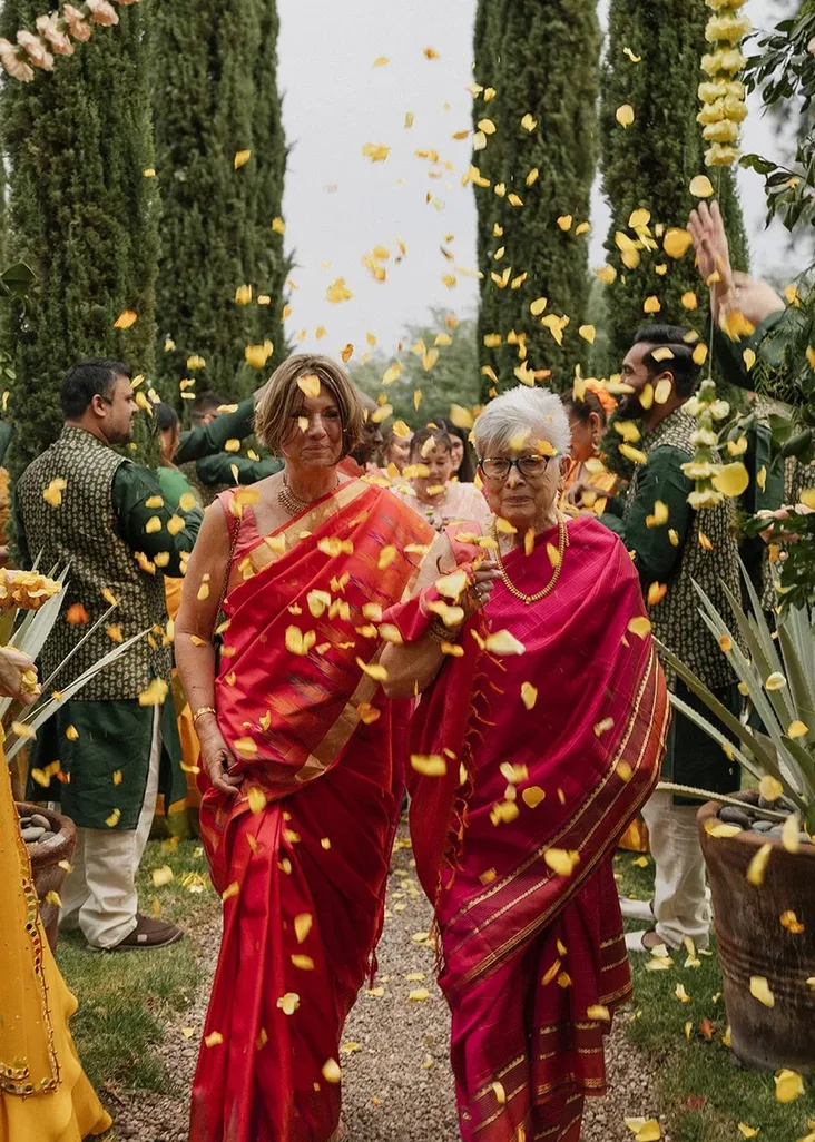 Wedding guests in vivid saris walking through a shower of yellow flower petals
