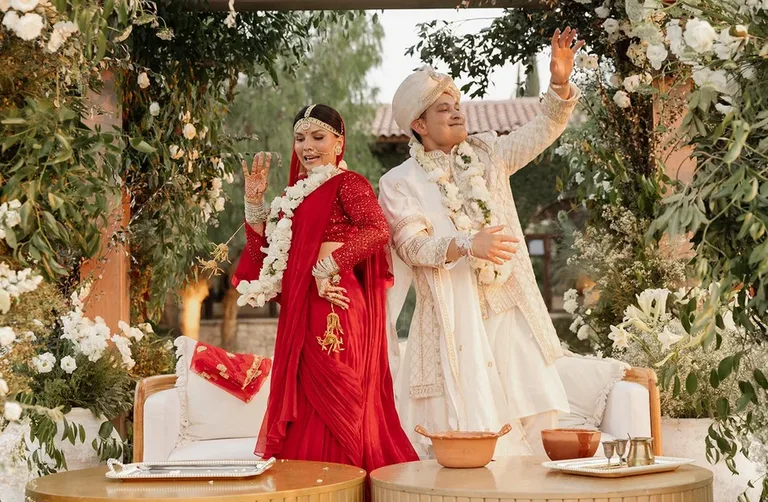 Newlyweds in traditional South Asian wedding attire celebrating beneath a lush floral structure