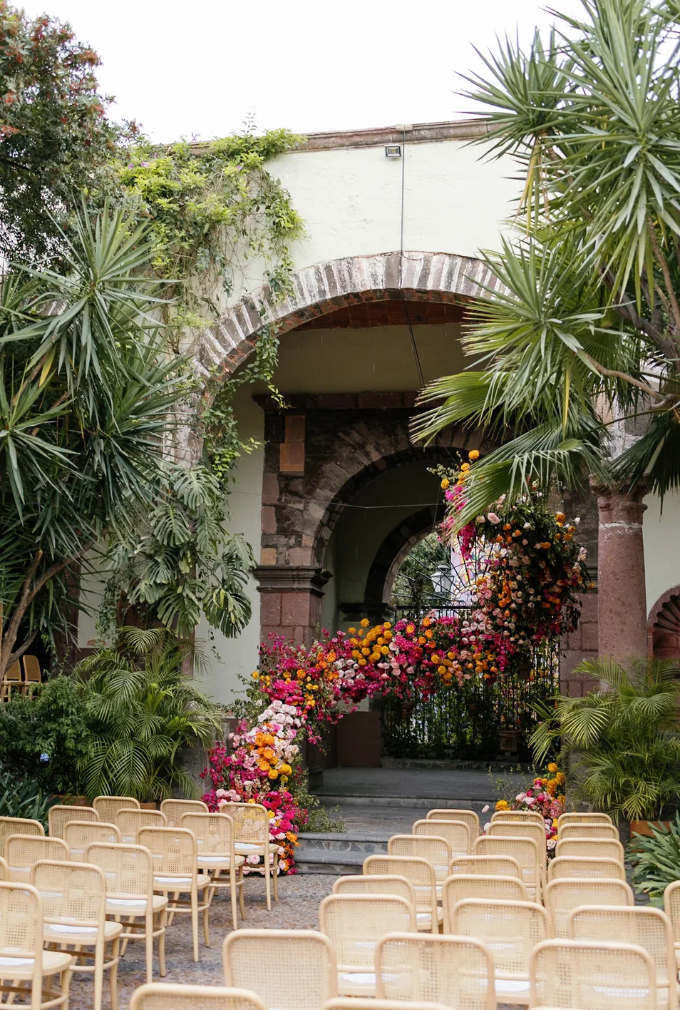 Courtyard wedding aisle leading to a vivid asymmetrical floral arch