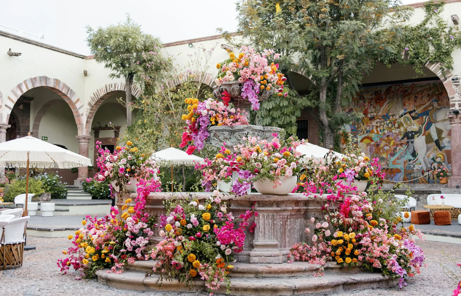 Historic courtyard fountain overflowing with vibrant pink, orange and yellow wedding flowers
