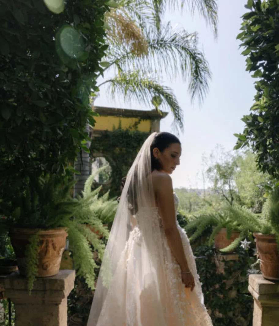 Bride in a lace gown and veil posing in a lush garden