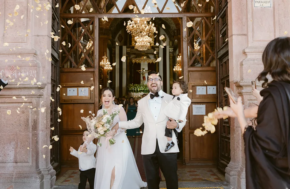 Newlyweds and their children celebrating beneath falling flower petals outside a church