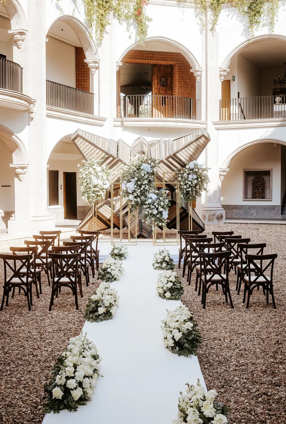 White floral ceremony aisle arranged in a light-filled arched courtyard