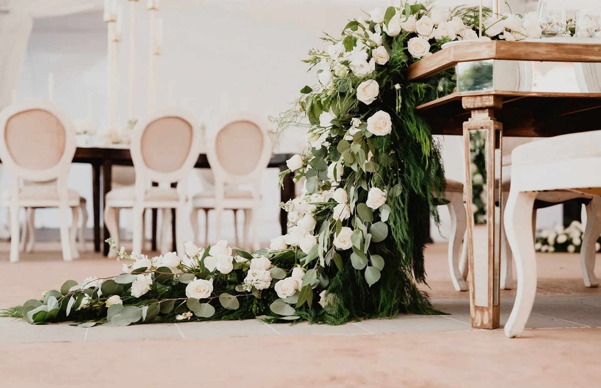 Cascading white roses and greenery decorating a mirrored wedding table